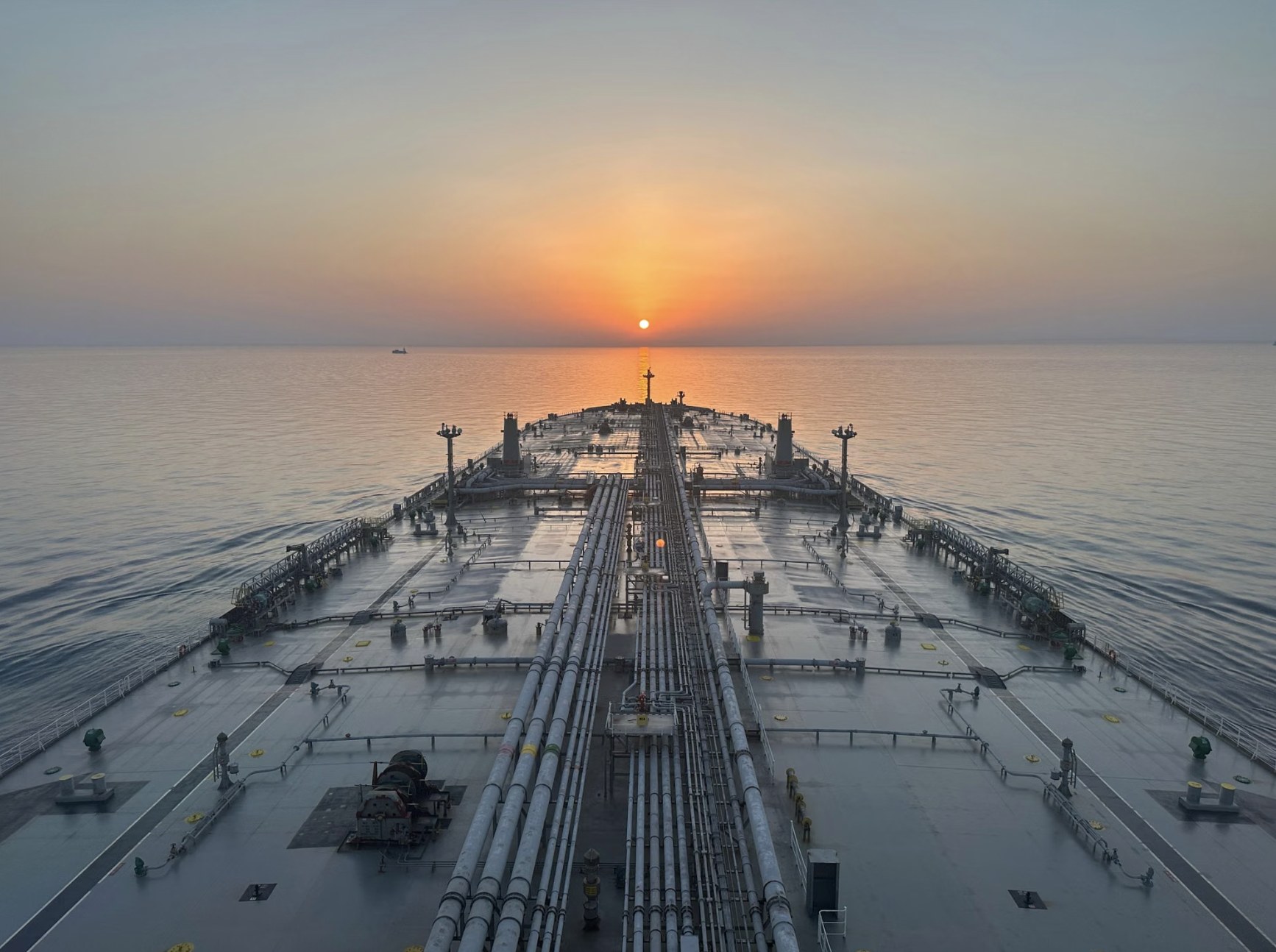Deck of a crude oil tanker at sea at sunrise, cargo manifolds running toward the bow